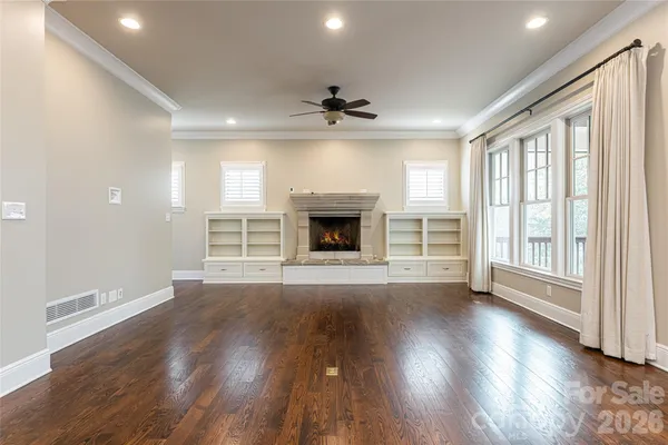 an empty room with wooden floor fireplace cabinet and windows