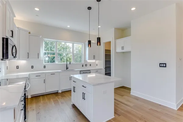 a large white kitchen with stainless steel appliances granite countertop a sink dishwasher a stove and white countertops with wooden floor