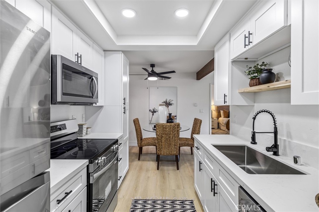 33852 Del Obispo Street, Unit 80 Dana Point, CA 92629 - Photo 6 of 36 a kitchen with stainless steel appliances a sink a stove top oven a chimney cabinets and a dining table