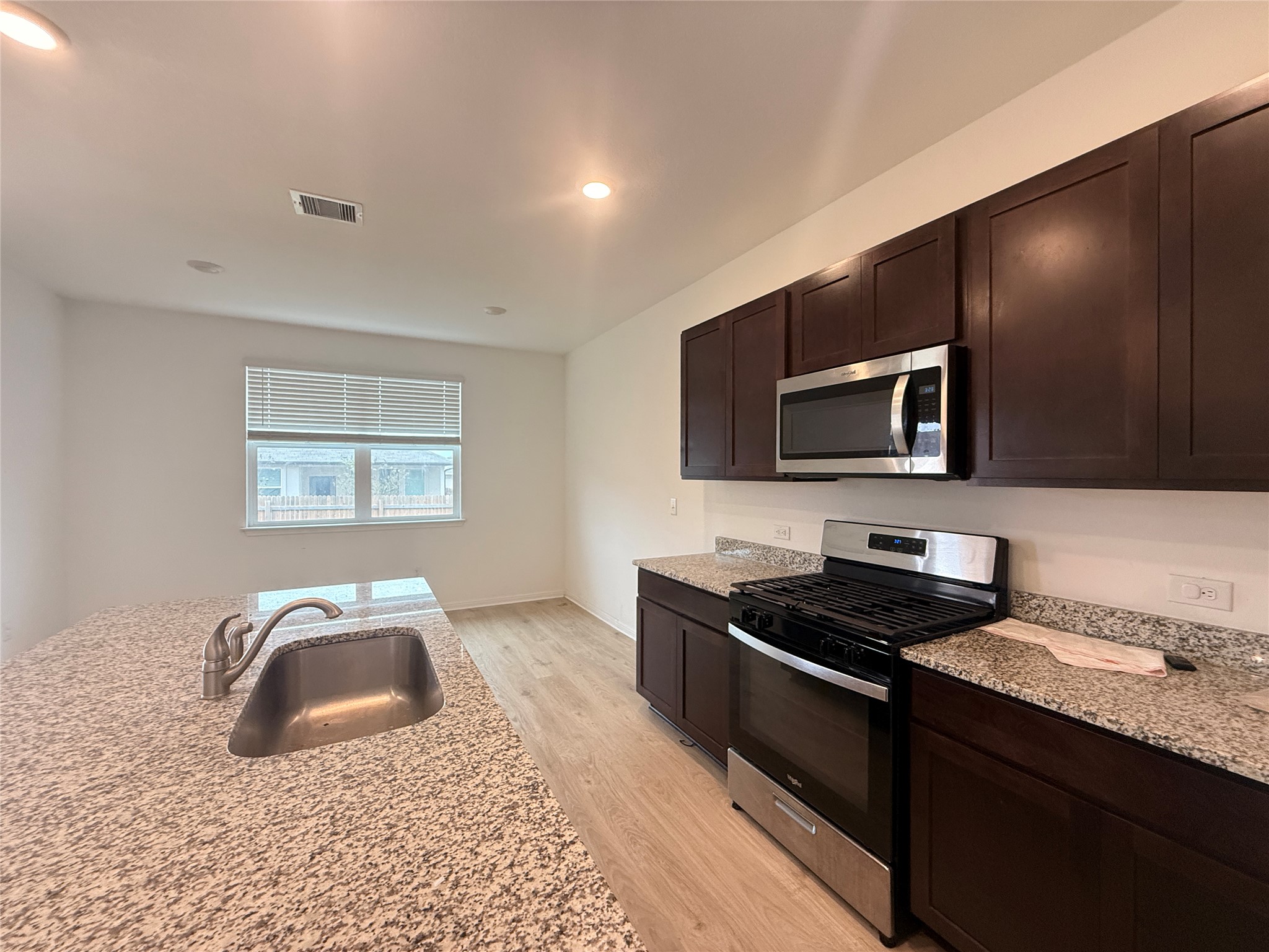 120 Calla Lane Georgetown, TX 78626 - Photo 4 of 19 Kitchen with stainless steel appliances, dark wood finish cabinetry, light stone countertops, light wood-style flooring, and recessed lighting