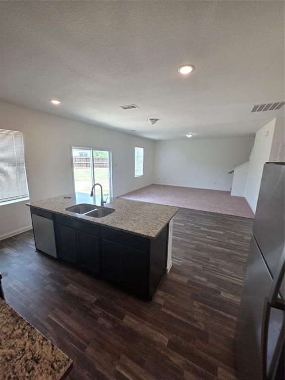 477 Bank Way Crowley, TX 76036 - Photo 30 of 39 Kitchen featuring fridge, an island with sink, dishwashing machine, light stone counters, and a textured ceiling