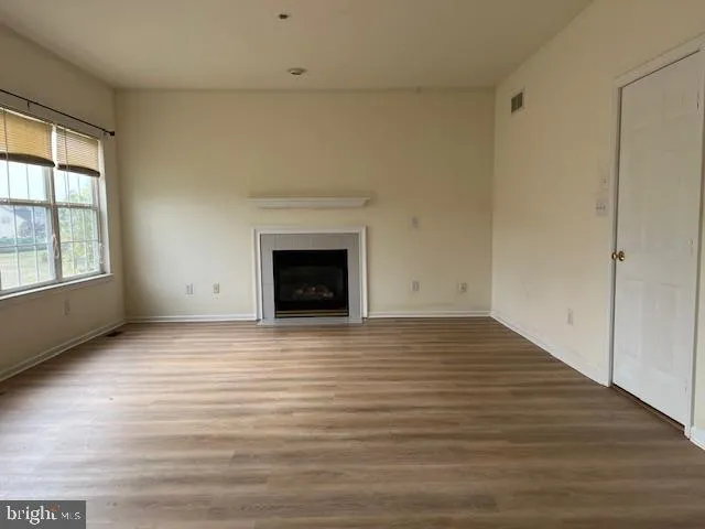 a view of an empty room with wooden floor fireplace and a window
