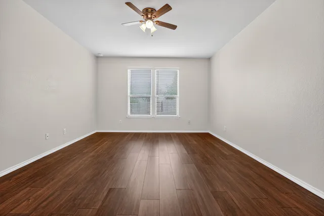 an empty room with wooden floor fan and windows