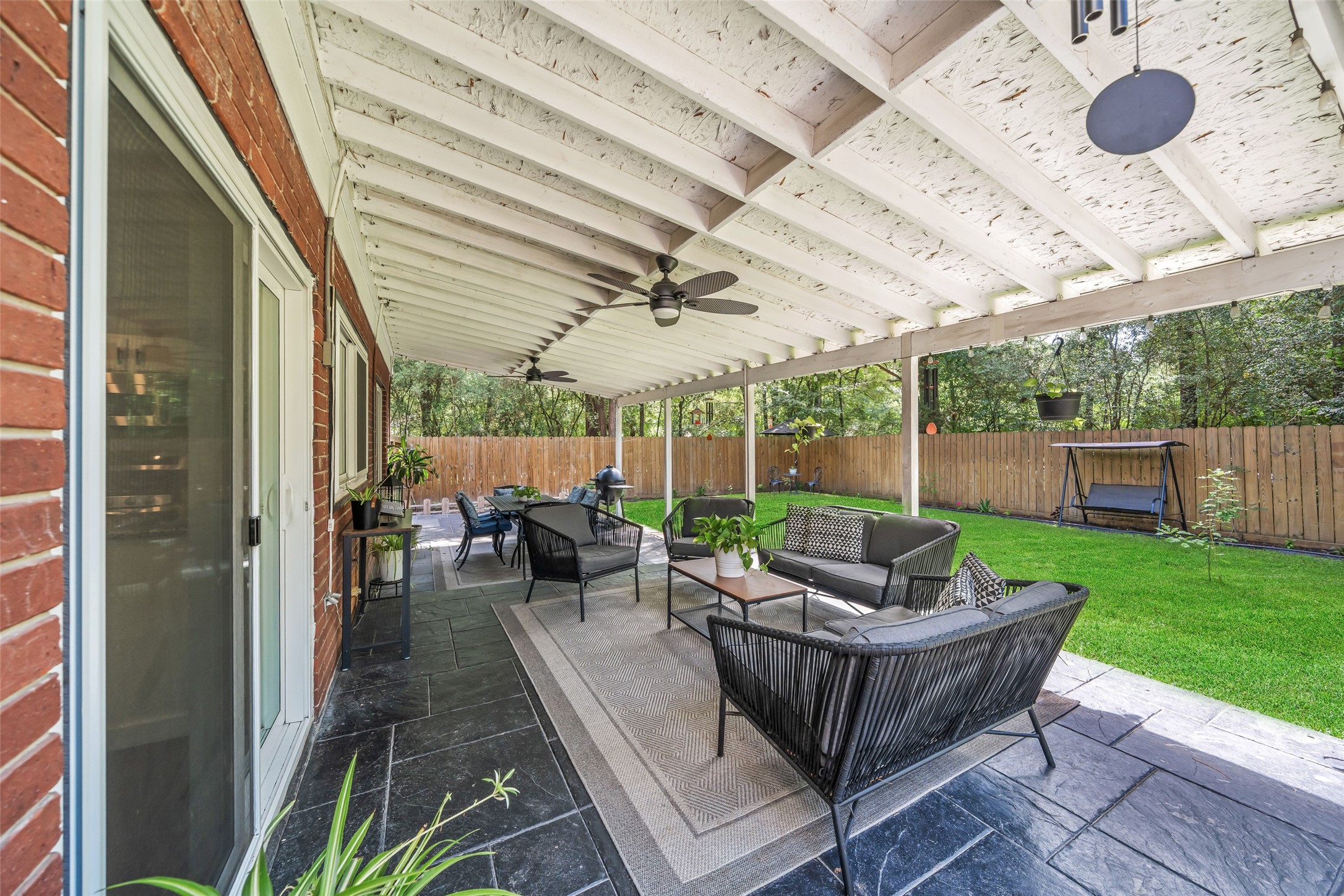 3 East Stony Bridge Circle Spring, TX 77381 - Photo 37 of 42 Spacious covered patio with comfortable seating area and a ceiling fan, overlooking a well-maintained backyard with a wooden fence, lush grass, and mature trees.