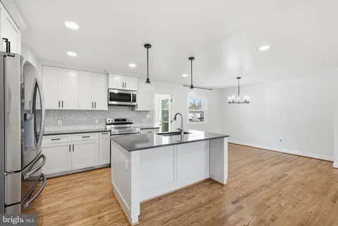 a kitchen with stainless steel appliances a stove a sink dishwasher a refrigerator and white cabinets with wooden floor