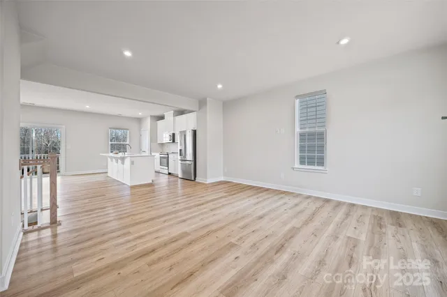 a view of empty room with wooden floor and kitchen