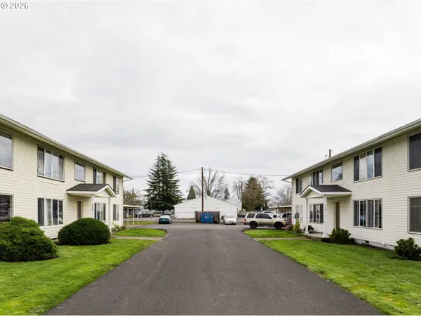 a view of a white house next to a yard with big trees