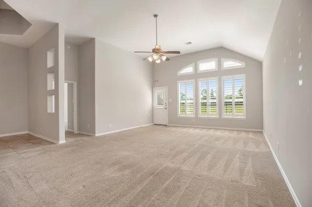 an empty room with chandelier fan and windows