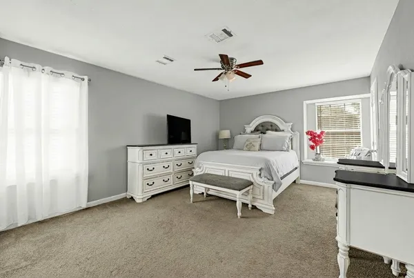 a spacious bedroom with a bed and a flat tv screen on the dresser