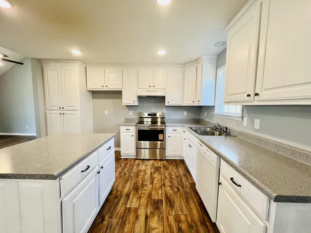 a large kitchen with stainless steel appliances granite countertop a stove a sink and white cabinets