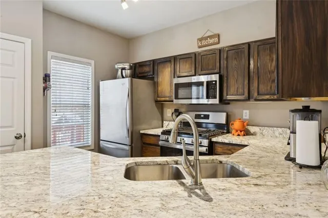 a kitchen with stainless steel appliances granite countertop a refrigerator a stove and a sink with wooden cabinets