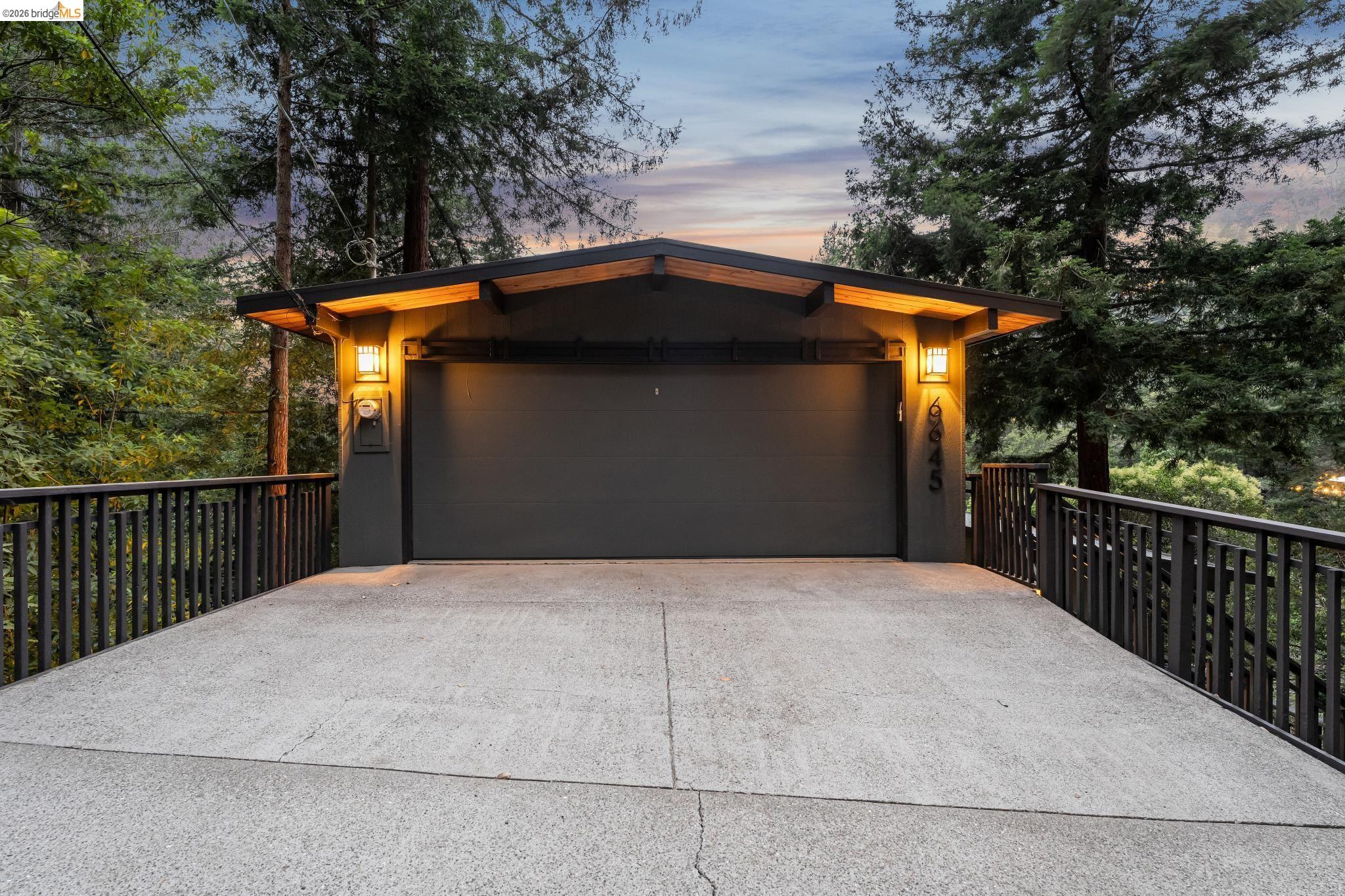 6645 Heather Ridge Way Oakland, CA 94611 - Photo 5 of 61 Attached garage with a flat panel door, concrete driveway, and exterior lighting fixtures