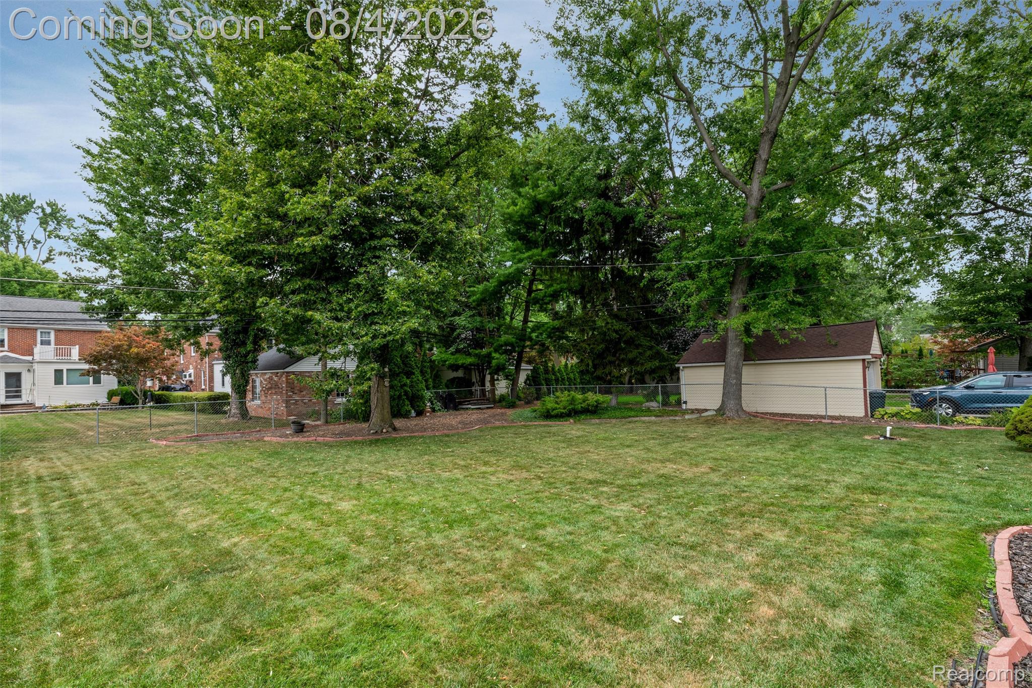 1729 Broadstone Road Grosse Pointe, MI 48236 - Photo 34 of 39 Expansive grassy yard featuring mature trees, a storage shed with a shingled roof, a chain-link fence, and a brick-built structure