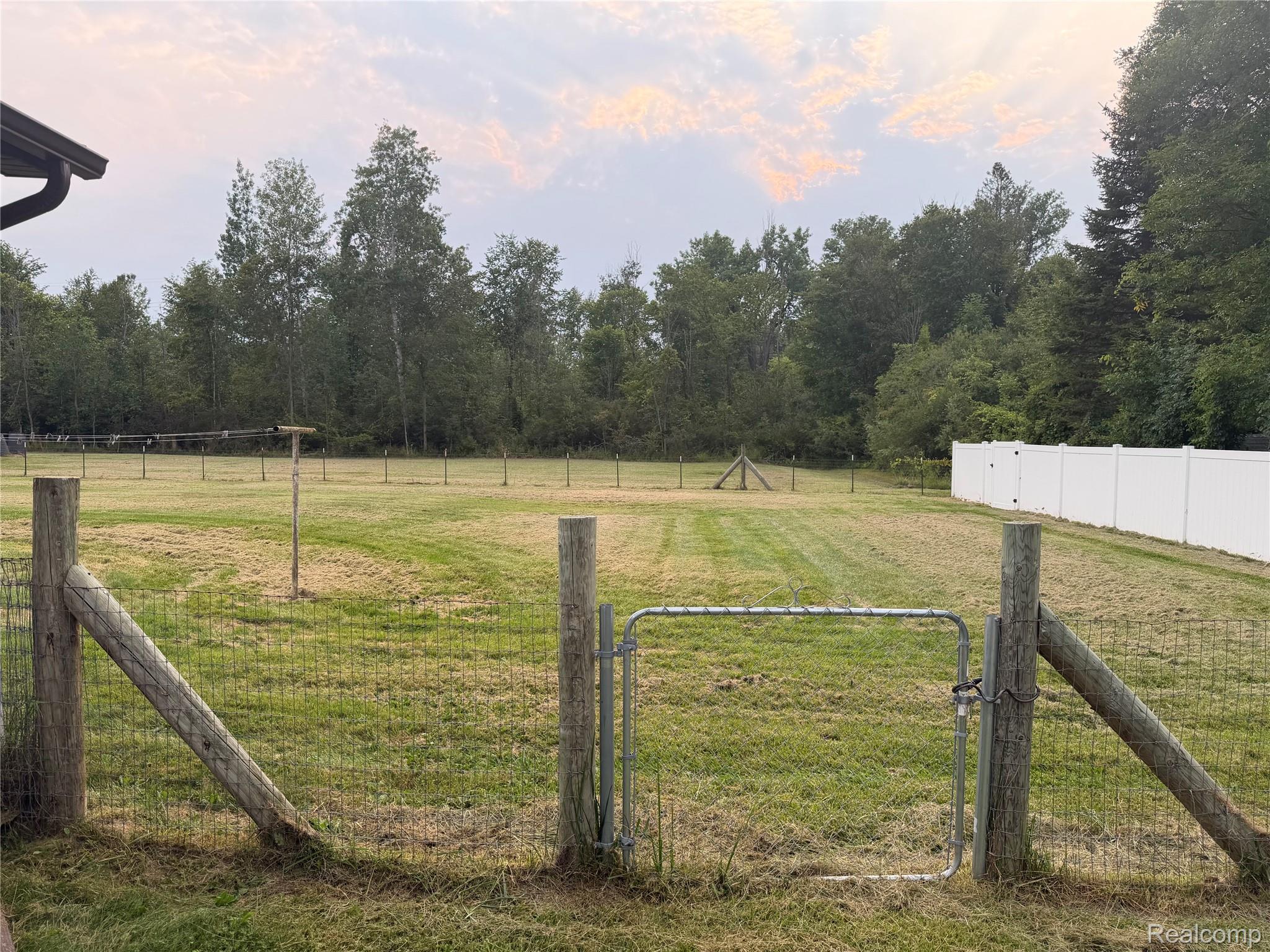 2402 Mertz Road Caro, MI 48723 - Photo 25 of 26 Expansive grassy yard with partial white privacy fencing, wire fencing, and a metal gate