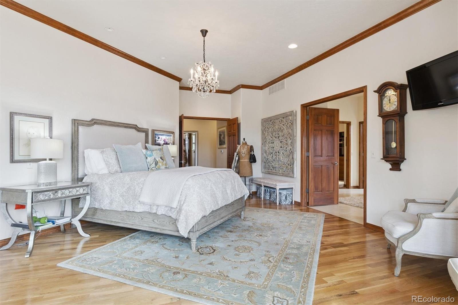 8061 Sugar Loaf Road Larkspur, CO 80118 - Photo 23 of 48 a bedroom with a bed wooden floor and chandelier