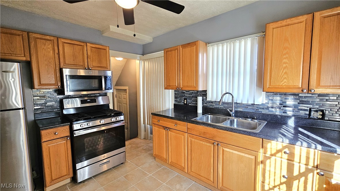 887 Rondel Road Cleveland, OH 44110 - Photo 15 of 34 Kitchen featuring light tile patterned flooring, appliances with stainless steel finishes, sink, backsplash, and a textured ceiling