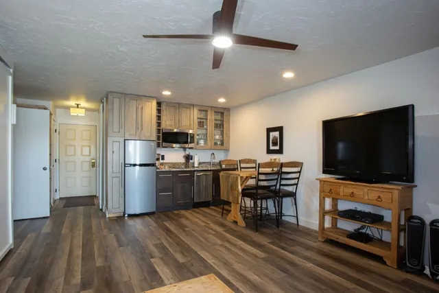 a kitchen with stainless steel appliances a refrigerator a stove top oven a sink dishwasher a dining table and chairs with wooden floor