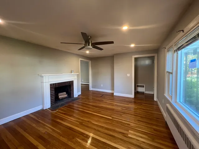 a view of an empty room with wooden floor fireplace and a window