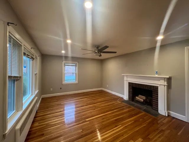 a view of an empty room with wooden floor fireplace and a window