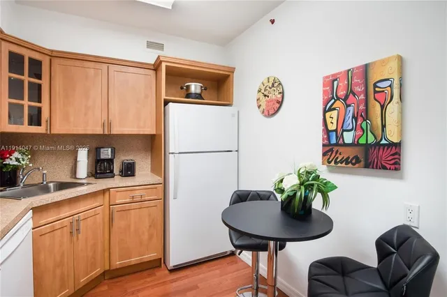 a kitchen with stainless steel appliances granite countertop a refrigerator a sink a stove a dining table and chairs with wooden floor