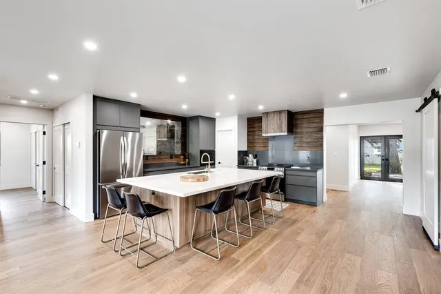 a kitchen with stainless steel appliances kitchen island granite countertop a refrigerator a stove a sink a dining table and chairs with wooden floor