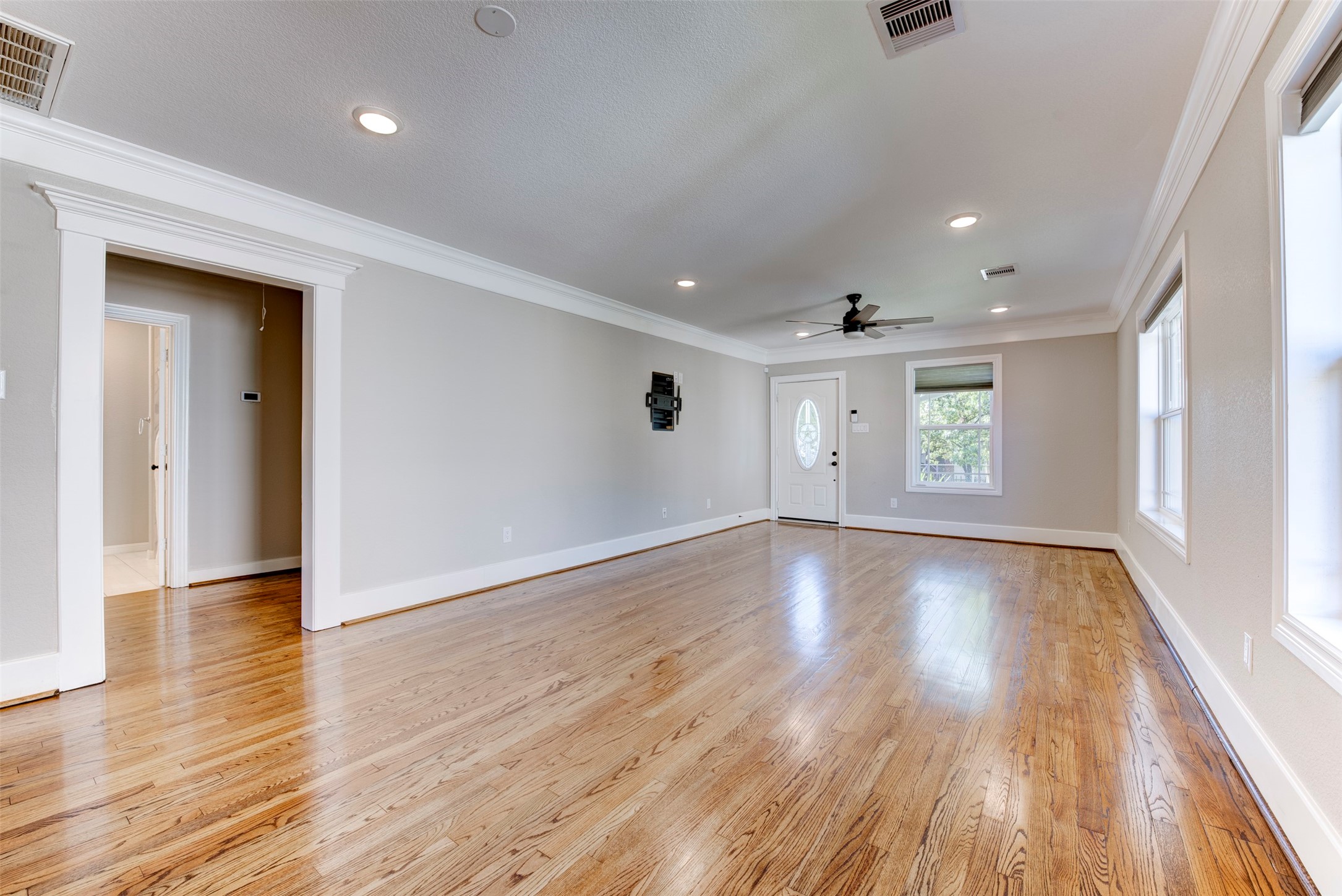 109 Dresden Street Houston, TX 77012 - Photo 7 of 43 This spacious living room features polished hardwood floors, neutral walls, and ample natural light from large windows. It includes recessed lighting, a ceiling fan, and elegant crown molding, offering a modern and inviting atmosphere.