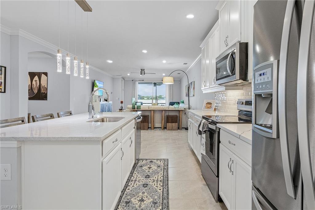 14618 Edgewater Circle Naples, FL 34114 - Photo 7 of 30 Kitchen featuring sink, light stone counters, a kitchen island with sink, light tile patterned floors, and stainless steel appliances