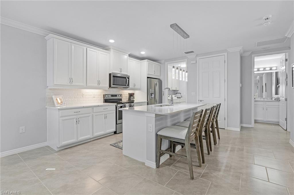 14618 Edgewater Circle Naples, FL 34114 - Photo 9 of 30 Kitchen with appliances with stainless steel finishes, decorative light fixtures, a center island with sink, crown molding, and white cabinets