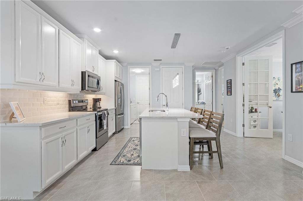 14618 Edgewater Circle Naples, FL 34114 - Photo 10 of 30 Kitchen with stainless steel appliances, white cabinetry, ornamental molding, tasteful backsplash, and light tile patterned floors