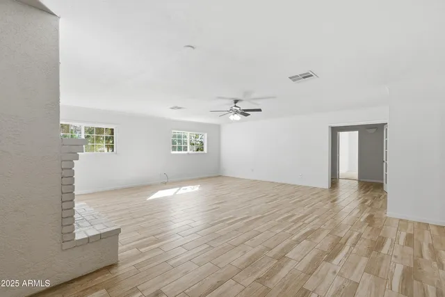 an empty room with wooden floor ceiling fan and windows