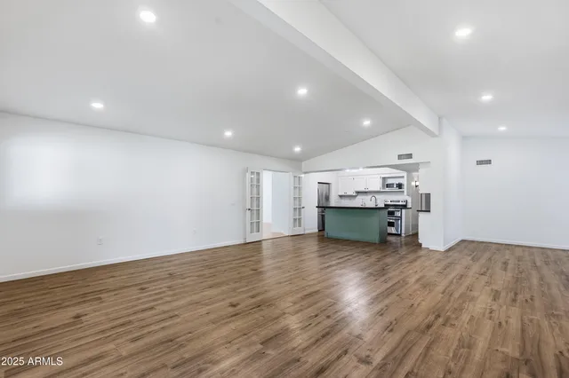 an empty room with wooden floor kitchen view and a window
