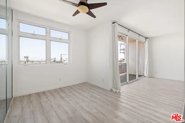 an empty room with wooden floor fan and windows