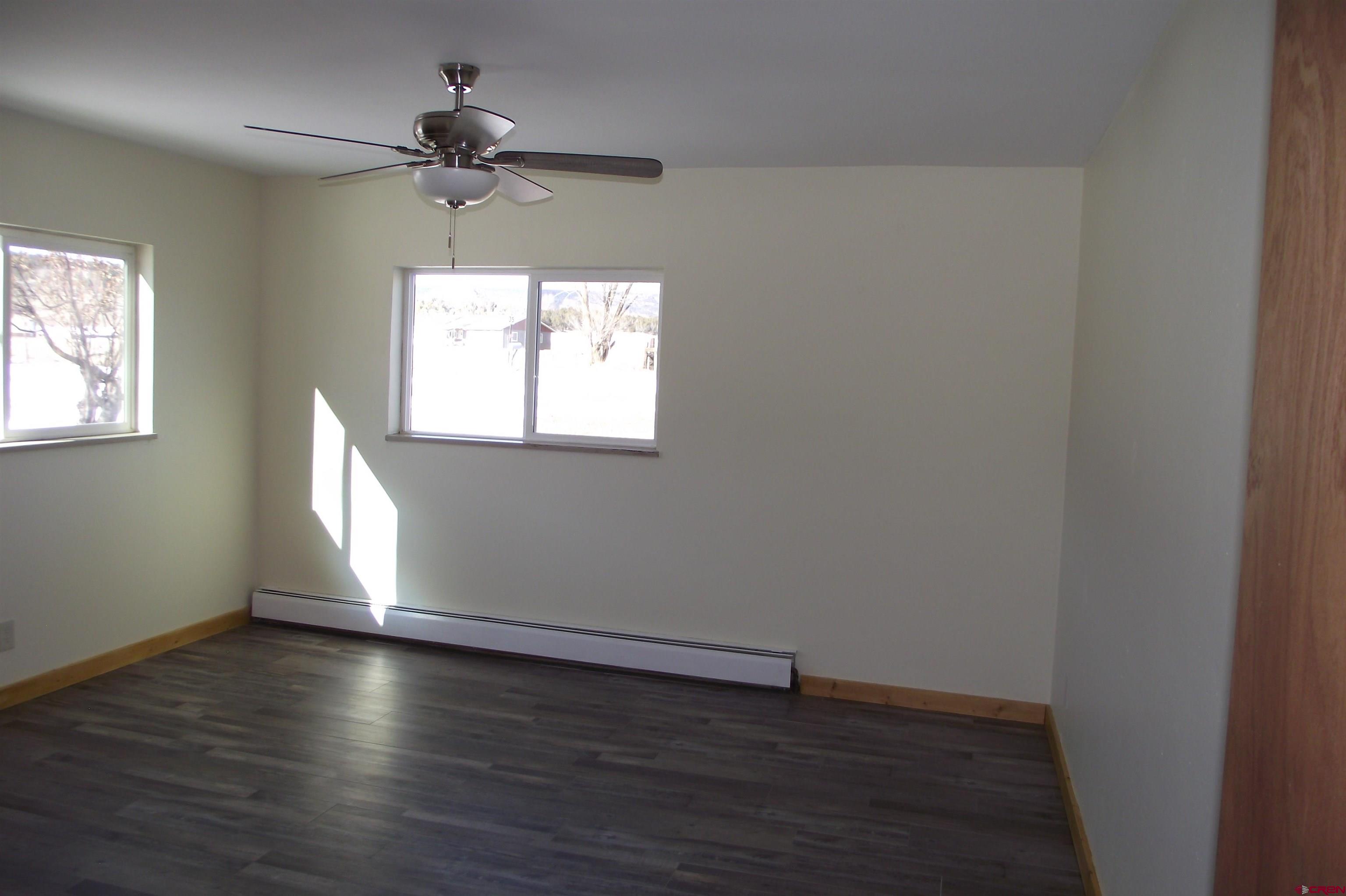 27434 Cedar Mesa Road Cedaredge, CO 81413 - Photo 23 of 36 an empty room with wooden floor chandelier fan and windows