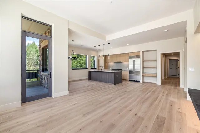 a view of an empty room with wooden floor and a kitchen