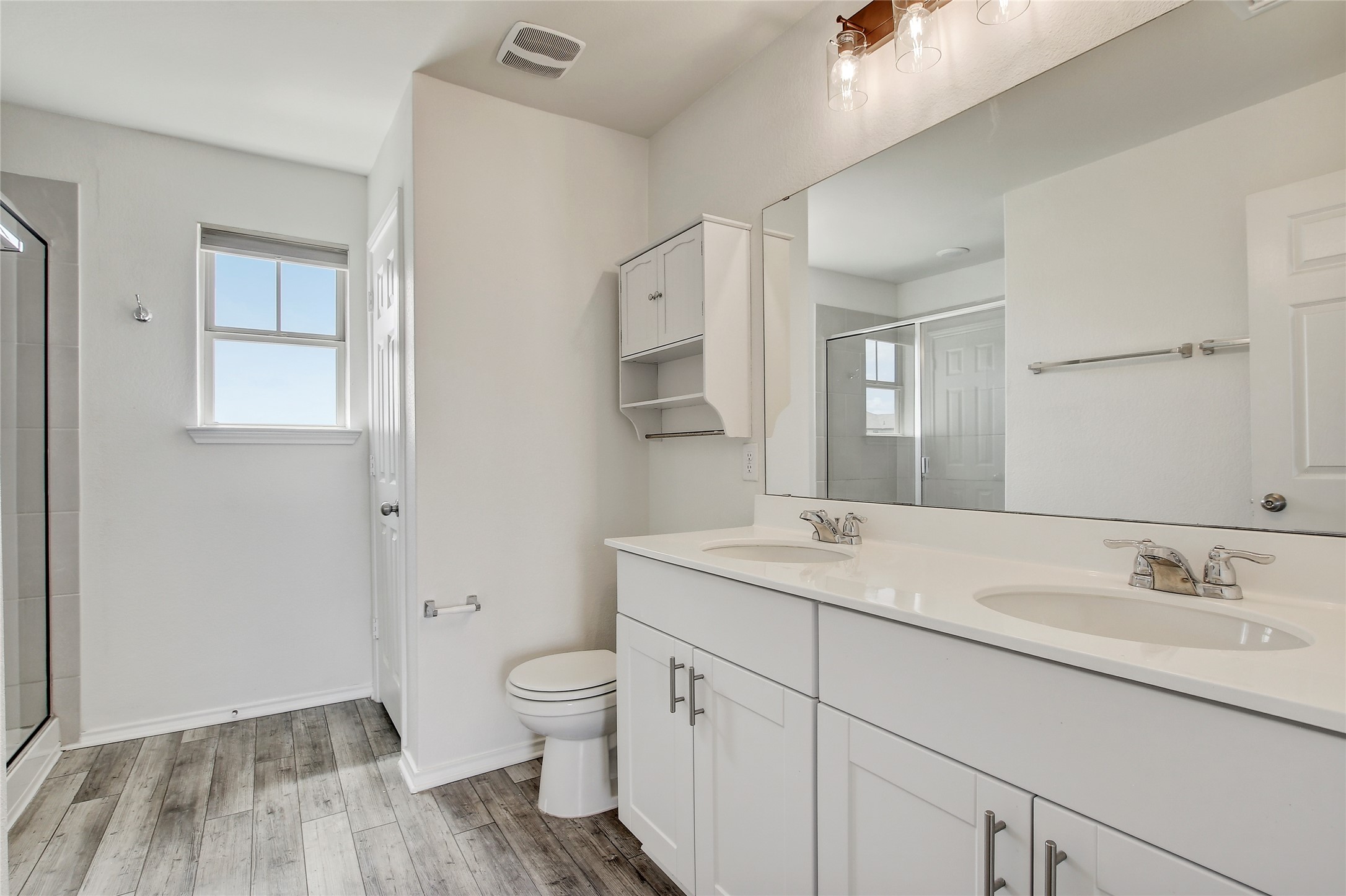 449 Stone Water Lane Jarrell, TX 76537 - Photo 12 of 18 Bathroom featuring wood-finish flooring, a double vanity with white cabinetry and integrated sinks, a large wall-mounted mirror, and a glass-enclosed shower