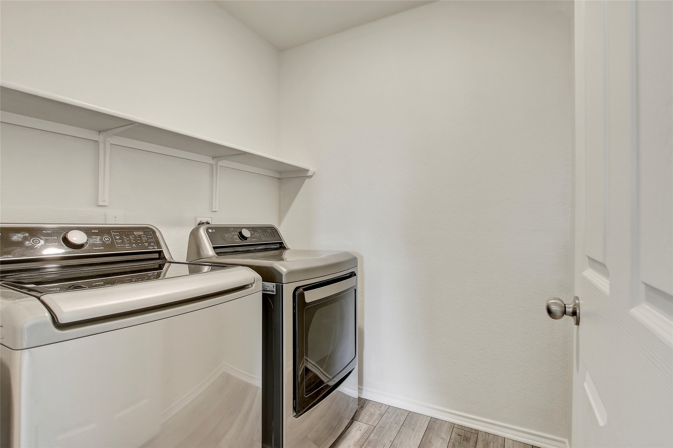 449 Stone Water Lane Jarrell, TX 76537 - Photo 14 of 18 Laundry area featuring a long white shelf, light wood-finish flooring, and a white paneled door with a brushed nickel doorknob