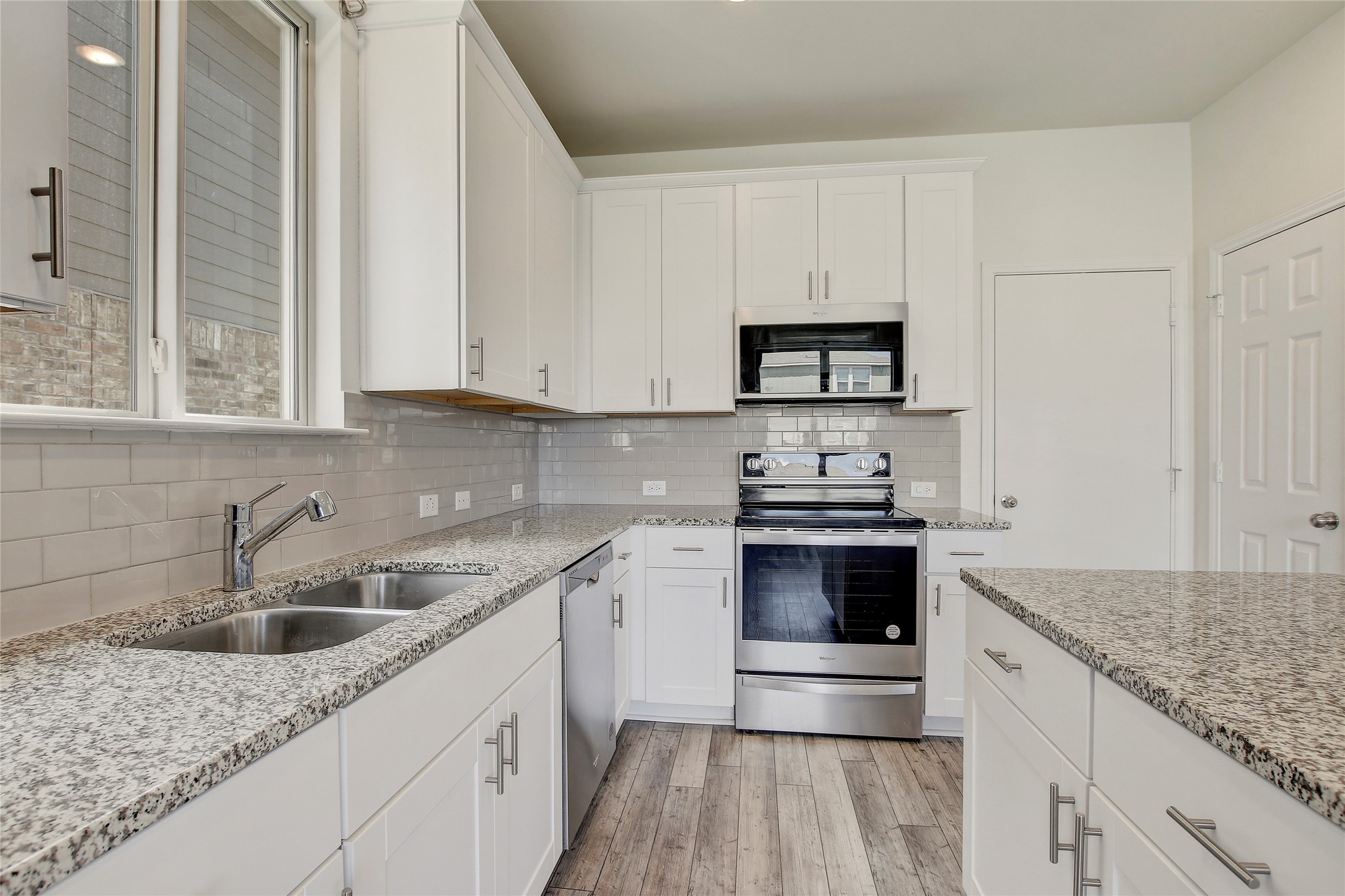 449 Stone Water Lane Jarrell, TX 76537 - Photo 5 of 18 Modern kitchen featuring white shaker cabinetry, speckled countertops, stainless steel appliances, a subway tile backsplash, and wood-finish flooring