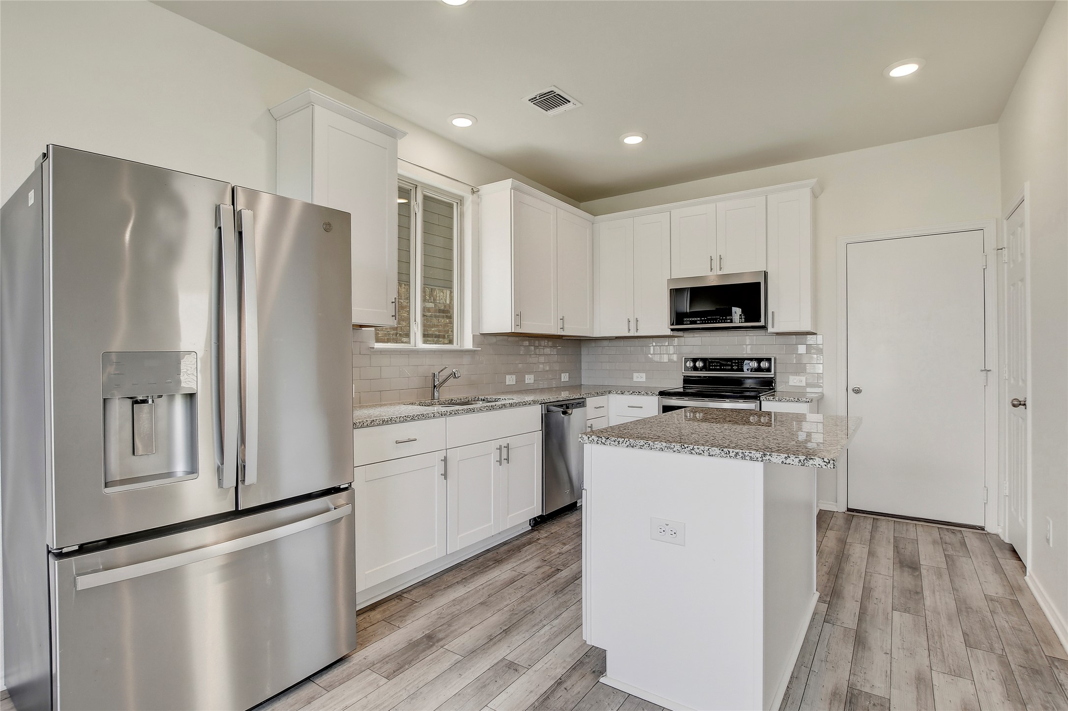 449 Stone Water Lane Jarrell, TX 76537 - Photo 7 of 18 Kitchen featuring white shaker cabinetry, stainless steel appliances, a center island with a granite-finish countertop, and wood-finish flooring