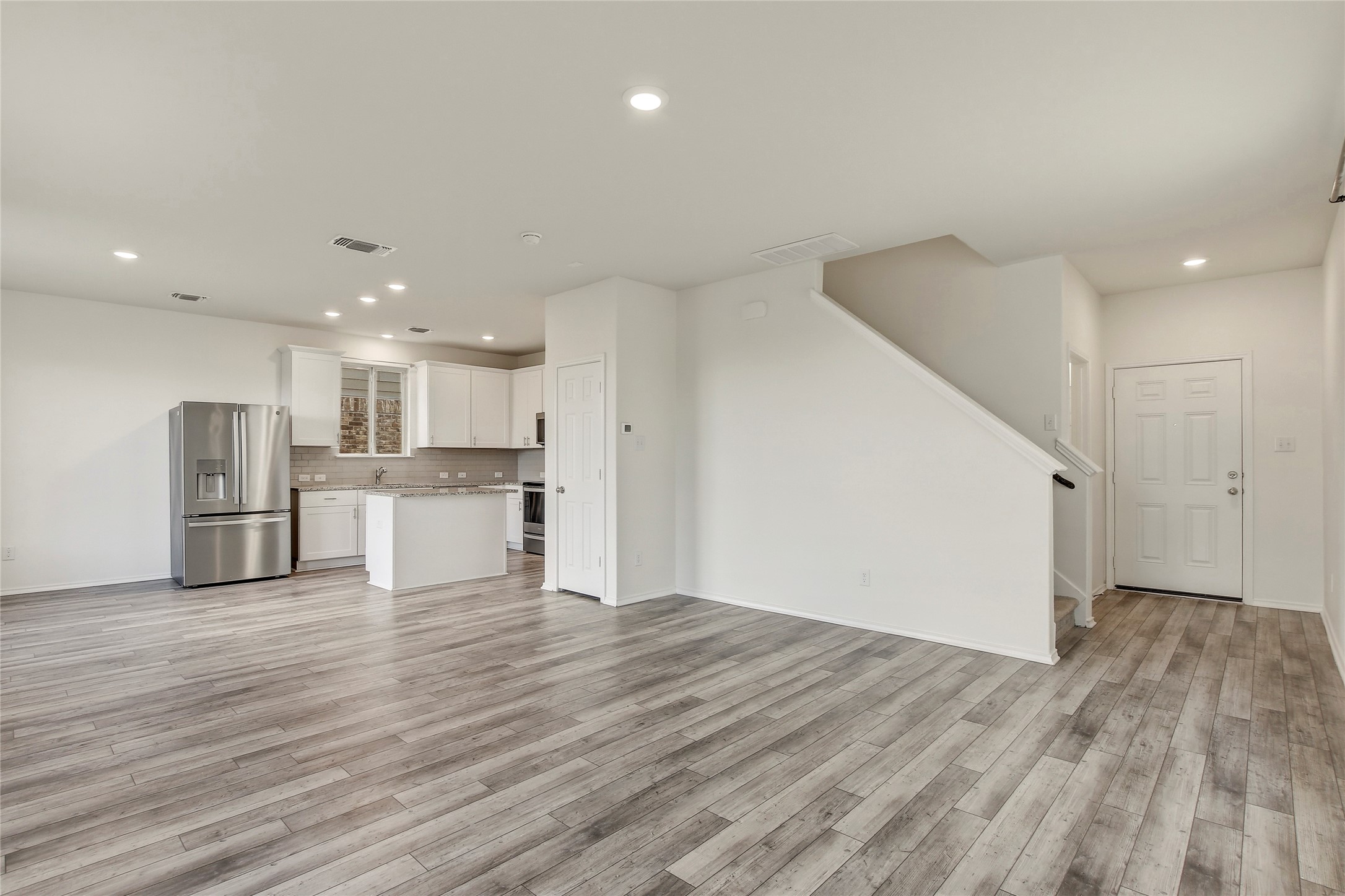 449 Stone Water Lane Jarrell, TX 76537 - Photo 9 of 18 Open-concept living area featuring wood-finish flooring, recessed lighting, and a kitchen with white cabinetry, stainless steel appliances, and a central island