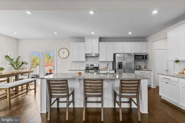 a kitchen with stainless steel appliances granite countertop a stove top oven a refrigerator a dining table and chairs with wooden floor