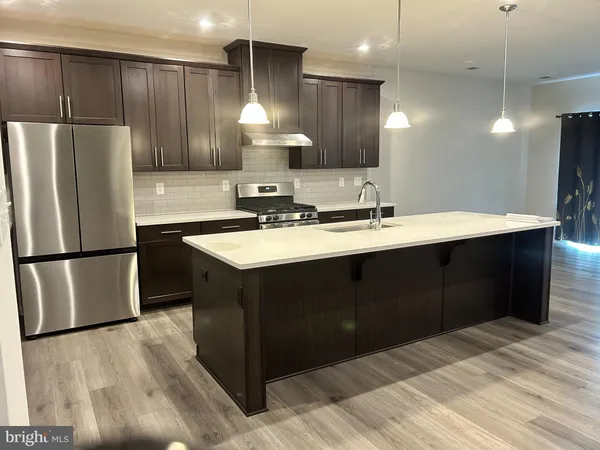 a kitchen with stainless steel appliances a sink a refrigerator a center island and a wooden floor