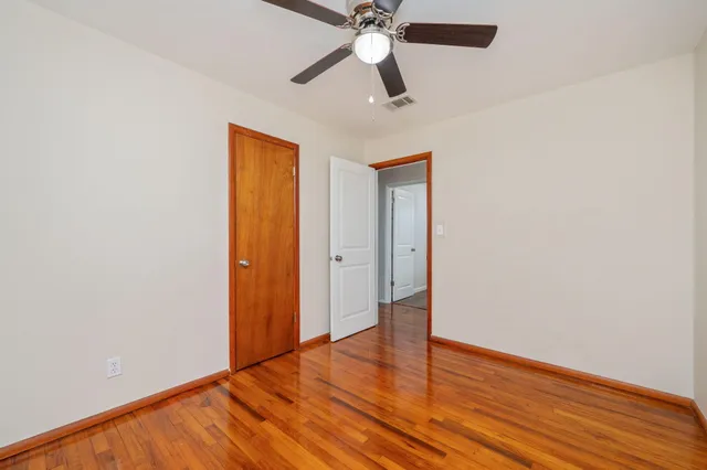 an empty room with wooden floor ceiling fan and windows