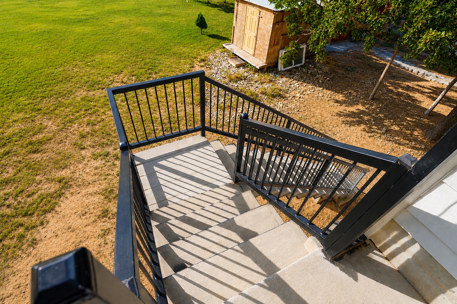 158 Buena Fortuna Road Elgin, TX 78621 - Photo 15 of 40 Concrete stairs with robust black railings descend into a landscaped yard featuring a rustic shed.