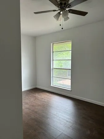 an empty room with wooden floor fan and windows