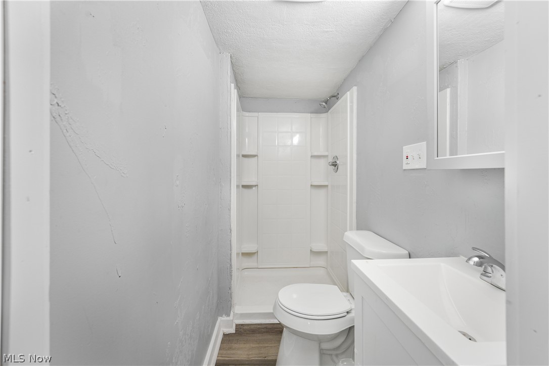 885 Wales Road Northeast Massillon, OH 44646 - Photo 5 of 34 Compact bathroom featuring a shower stall, toilet, vanity with integrated sink, wood-finish flooring, and a mirrored medicine cabinet