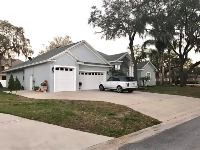 a view of a white house in front of a yard with large trees