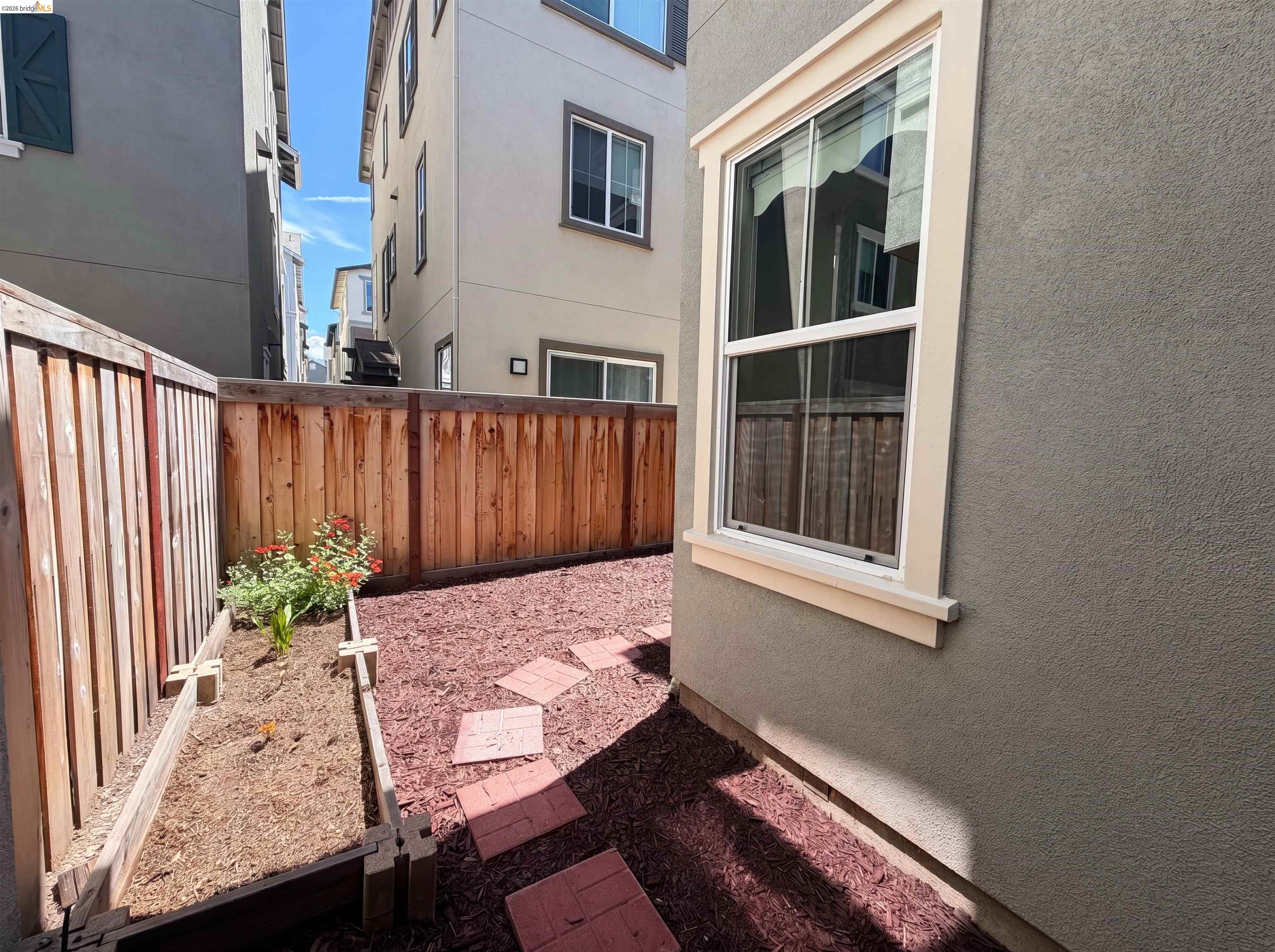 9034 Rudder Way Newark, CA 94560 - Photo 12 of 38 Private outdoor space featuring a wood fence, raised garden bed with plantings, red mulch ground cover, and stepping stones