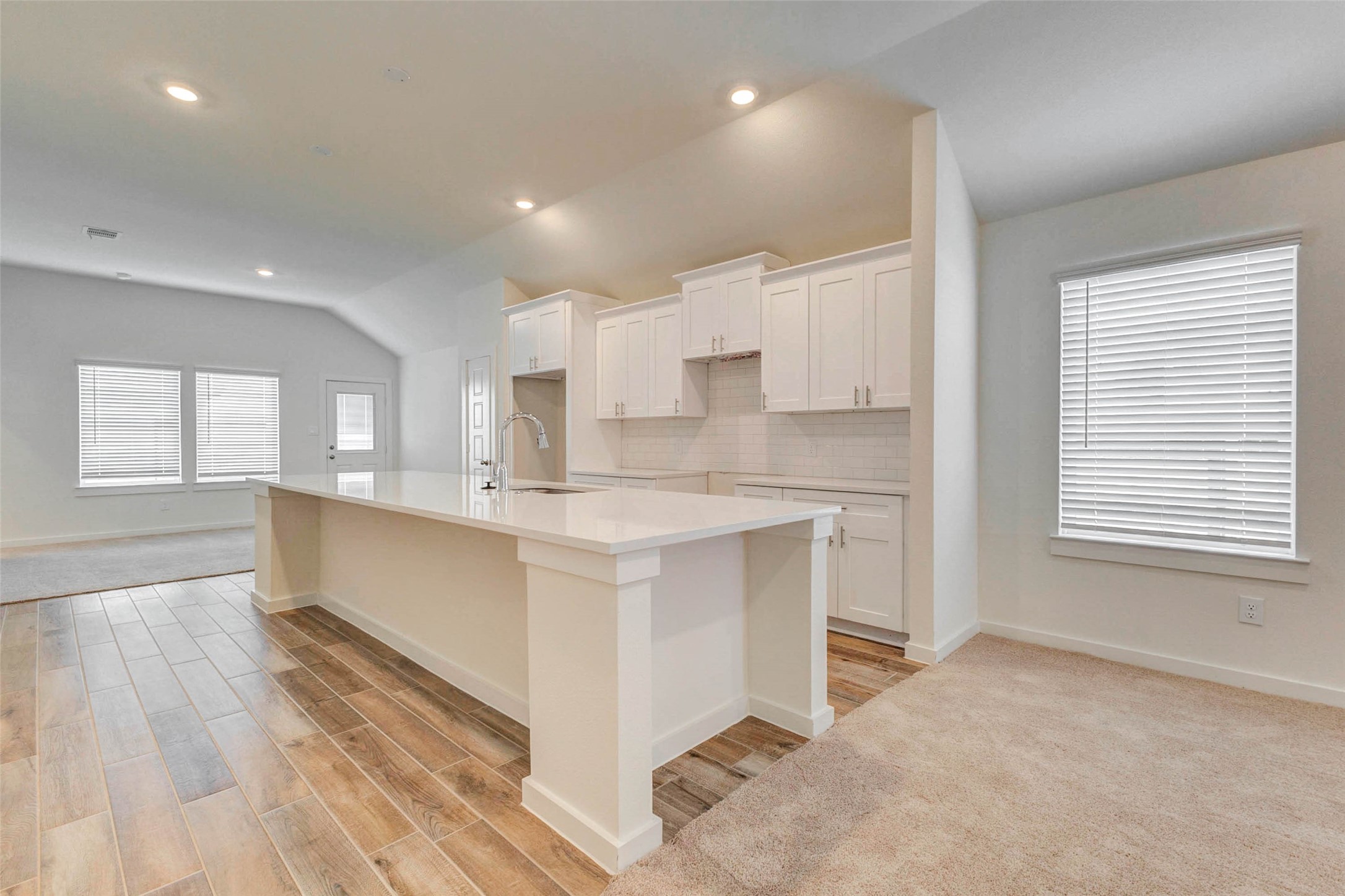 6475 Escondido Drive Rosharon, TX 77583 - Photo 14 of 32 The kitchen features a large island with a sleek countertop, white cabinetry, subway tile backsplash, and warm wood-look tile flooring. Open to the living and dining areas, this bright space offers both style and function with plenty of room for meal prep, casual dining, and gathering.