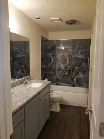 a bathroom with a granite countertop sink a toilet a mirror and bathtub