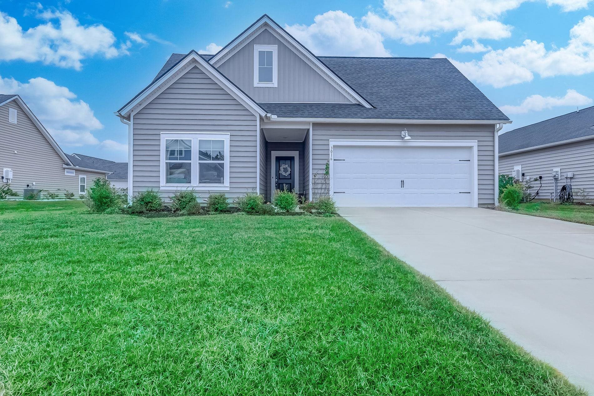 View of front of home with a front yard, an attached garage, roof with shingles, driveway, and board and batten siding